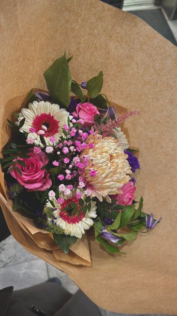 A vibrant bouquet of fresh flowers arranged with a variety of blooms including pink roses, white daisies with pink centers, cream-colored carnations, and small purple and pink filler flowers. The arra