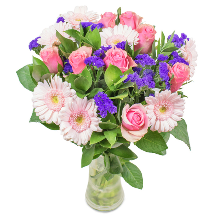 In a graceful glass vase set against a pristine white expanse, this floral arrangement captures the classic beauty and welcoming personality of Herne Hill. Seven to nine softly blushed pink roses anchor the bouquet with their iconic spirals, petals tightly furled or just beginning to unfurl-symbols of love, promise, and heartfelt sentiment. Interspersed among them are several pale pink gerbera daisies, their broad, radiant faces and almost creamy centres evoking the simple splendour of Brockwell Park in full bloom. Vivid violet clusters of statice or limonium peek out between the larger flowers, lending a striking textured counterpoint and a richer depth as seen in local woodland edges. Lush, emerald green foliage, glossy and full, is artfully arranged to cradle and support the blooms. Visible stems in the clear vase and fresh water allude to same-day delivery freshness-perfect for birthdays, anniversaries, Mother's Day surprises, or as a cheerful statement for any Herne Hill home or office. With every bloom, the arrangement expresses celebration, elegance, and community warmth.