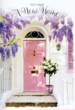 The photograph reveals a warm, inviting entrance that feels quintessentially Herne Hill: a pale pink door set into whitewashed walls, framed by a generous tumble of lavender wisteria. The door itself is smooth and freshly painted, its panels catching the light in gentle highlights that echo the softness of early evening along the streets by Brockwell Park. Overhead, wisteria pours down from above in loose, trailing clusters, each tiny blossom a shade of lilac or soft purple, creating a curtain of flowers that partially veils the doorway. To one side, a matching pink shutter balances the composition, adding depth and a sense of lived-in charm typical of these South London terraces. On the doorstep rests a single, thoughtfully crafted floral arrangement in a grey, metal bucket. Inside, creamy white roses bloom in abundance, their petals lush and velvety, unfurling in spirals that give the arrangement a full, generous look. Delicate stems of green foliage weave between the roses, providing gentle contrast and a feeling of freshness. A pink ribbon encircles the bucket, tied into a soft bow whose tails fall gracefully, repeating the pastel tones of the entrance. The light in the scene is soft and warm, casting gentle shadows that make the petals, vines, and brickwork feel almost tangible. Everything about the image suggests celebration and reassurance: a housewarming gift delivered to a new address in Herne Hill, quietly waiting at the door to greet its owners with the scent of roses and wisteria, and with the unspoken promise that this place, from the very first step, already feels like home.